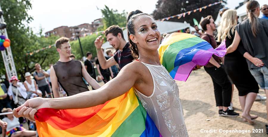 Kvinde danser til Copenhagen Pride med et regnbuefarvet flag om skulderne